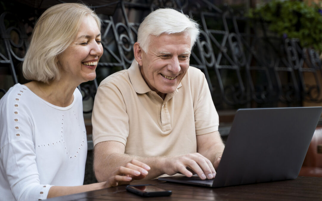 senior couple smiling as they work on a laptop