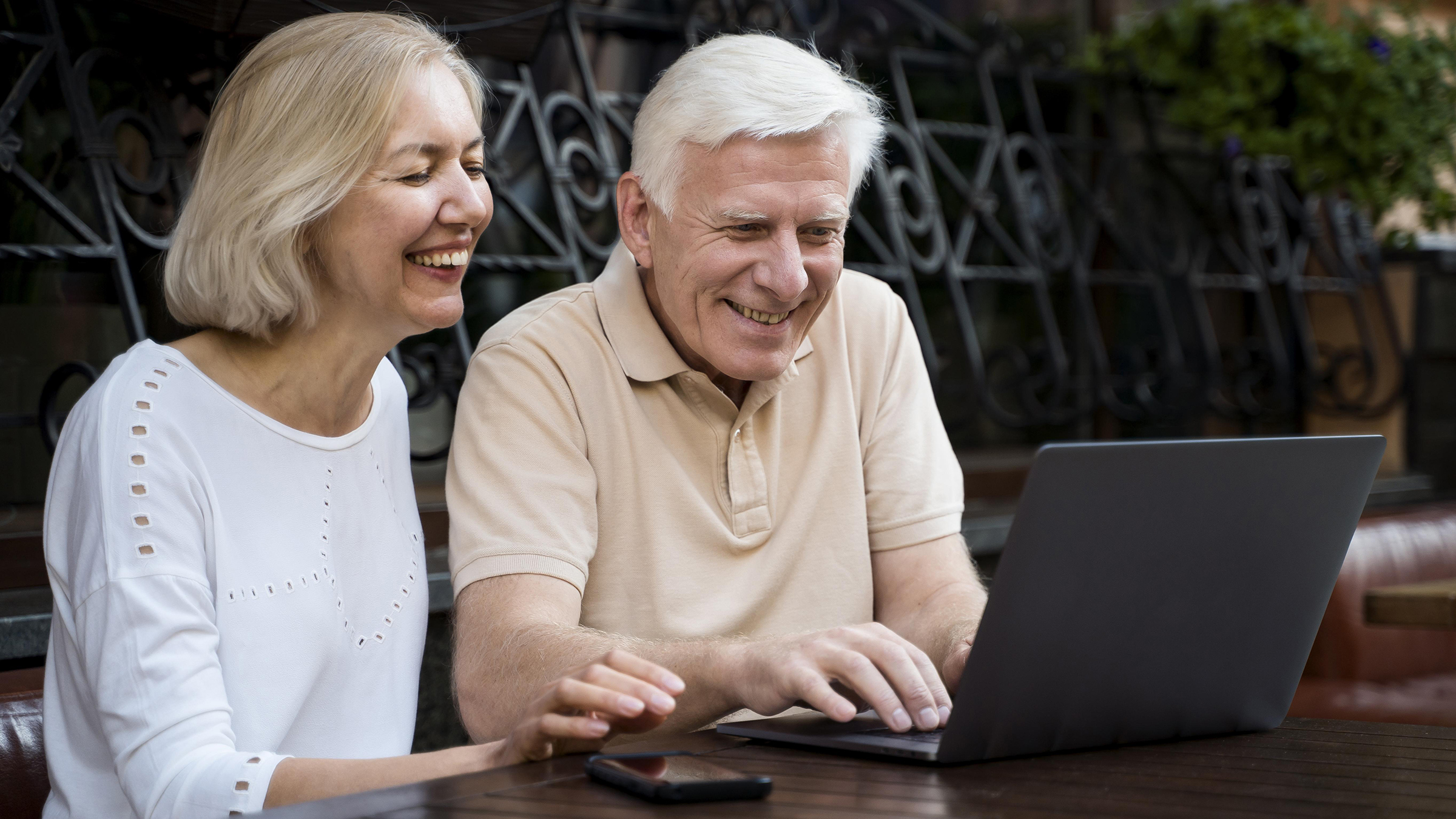 senior couple smiling as they work on a laptop