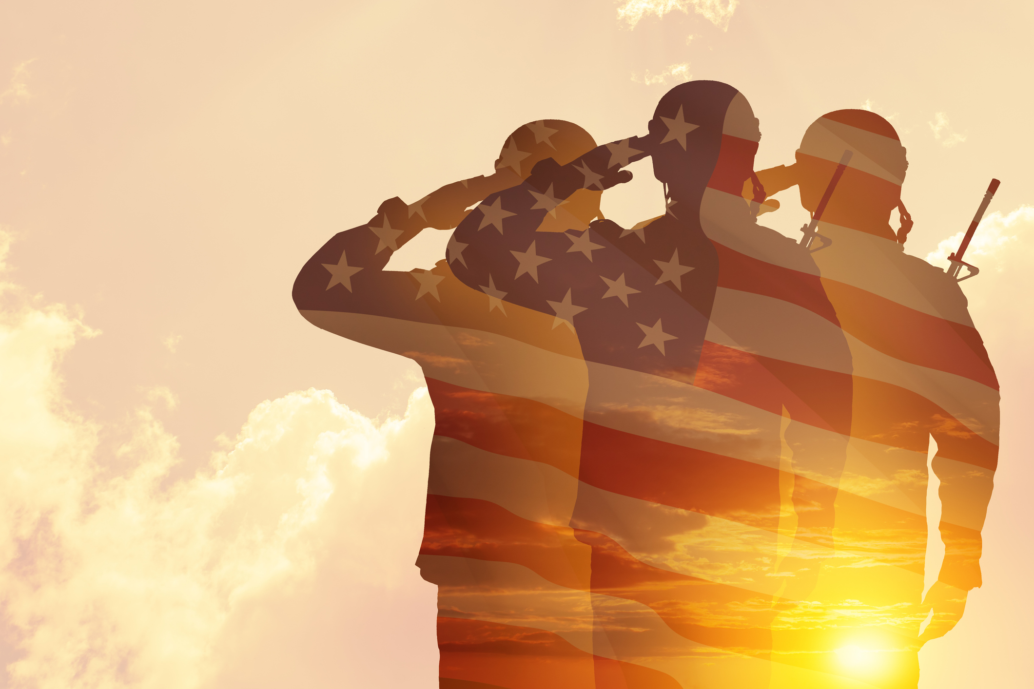 Silhouettes of soldiers with print of sunset and USA flag saluting on a background of light sky.