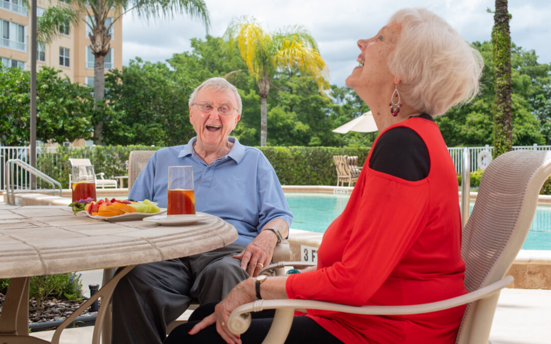 A couple laughs together while sitting by the pool on The Mayflower at Winter Park's lush campus.